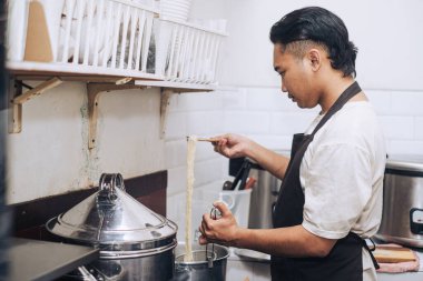 Önlüklü bir Güneydoğu Asyalı şef bokeh arkaplanlı erişte pişiriyor.