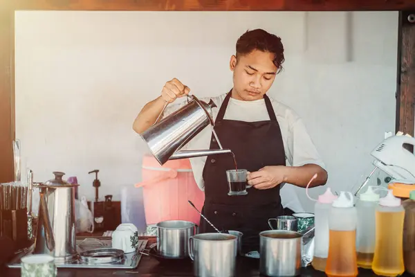 Önlüklü Güneydoğu Asyalı bir barista geleneksel Singapur kahve demliğinden kahve dolduruyor.