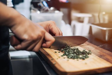 Tahta kesme tahtasının arka planında pırasa kesen bir elin yakın çekimi.