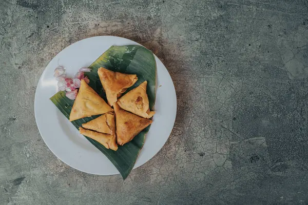 Kızarmış Samosa. Beyaz tabakta geleneksel Hint yemekleri ve beton bir masada soğanlar. Düz konum, üstten görünüm açısı ve sol taraftaki nesne..