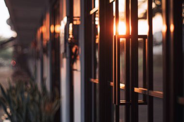 Siyah alüminyum ve camdan yapılmış kırmızı güneş ışığı ve bokeh arka planlı modern bir evin kapısı.