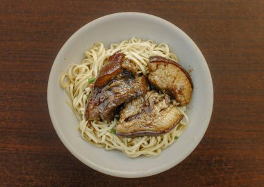 Ahşap bir masada soya soslu domuz göbeği ile kaplı bir kase Çin eriştesi. Düz yatış, üstten veya üstten görünüm açısı.