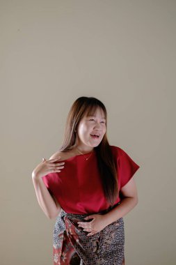 Geleneksel Endonezya Batik kıyafetli Güneydoğu Asyalı bir kadın, elini omzuna atıyor ve izole bir arka planda sağ tarafa ve mutlu bir yüze bakıyor. Dikey çekim.