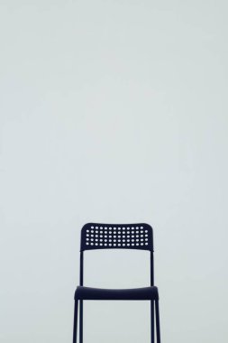 Arka plan olarak beyaz bir duvara yaslanmış minimalist siyah bir sandalye.