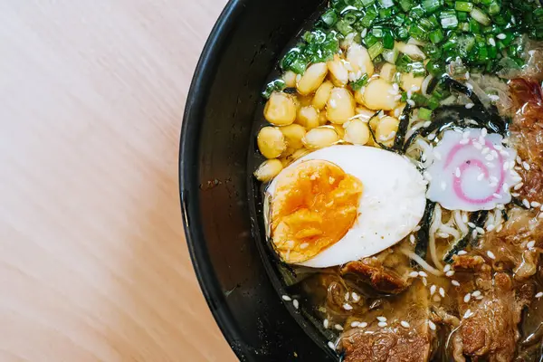 Japon Ramen 'in mısır, pırasa, yarım yumurta, sığır eti, nori ve narutomaki ile çekilmiş düz bir fotoğrafı. Yemek çubukları siyah kasede. Japon geleneksel yemeği.