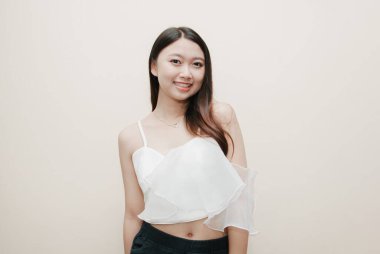 Tecrit edilmiş güzel bir Asyalı kadının gülümseyen yüzü. Süslü beyaz bluz ve siyah pantolon giyiyor..