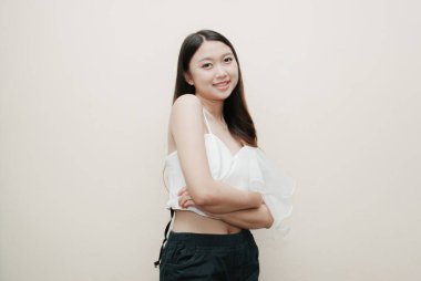 Tecrit edilmiş güzel bir Asyalı kadının gülümseyen yüzü. Süslü beyaz bluz ve siyah pantolon giyiyor..