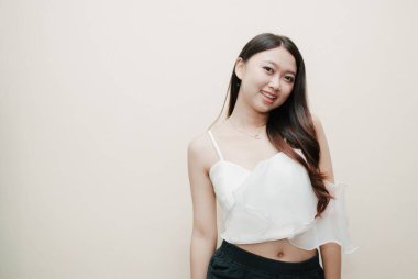 Tecrit edilmiş güzel bir Asyalı kadının gülümseyen yüzü. Süslü beyaz bluz ve siyah pantolon giyiyor..