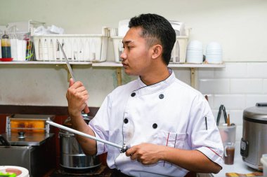 Genç profesyonel Asyalı şef ustalıkla bir bıçağı çelikle biler.