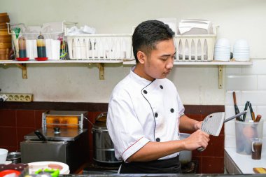 Genç profesyonel Asyalı şef ustalıkla bir bıçağı çelikle biler.