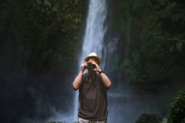 Gezgin bir adam şelalede kamera kullanarak fotoğraf çekiyor.