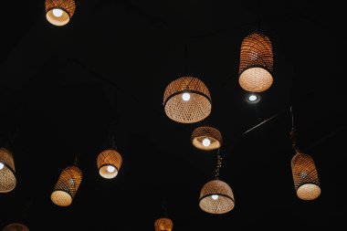 Ilık ışıkları ve koyu tavanı olan örülmüş rattan lambalar.