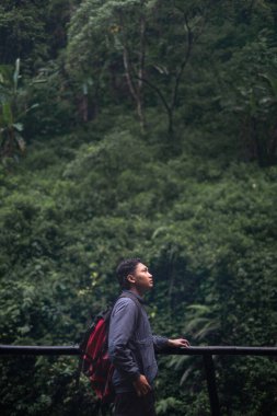 Güneydoğu Asyalı bir adam sırt çantasıyla tropikal ormanda yürüyüş yapıyor. Seyahat fotoğrafçılık konsepti.