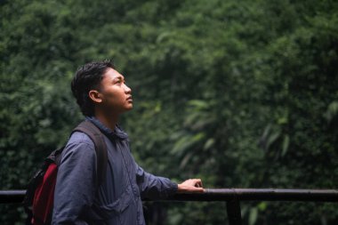 Güneydoğu Asyalı bir adam sırt çantasıyla tropikal ormanda yürüyüş yapıyor. Seyahat fotoğrafçılık konsepti.