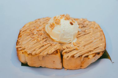 Karamel soslu tost ekmeği ve üzerine beyaz tabakta fındık serpiştirilmiş vanilyalı dondurma.