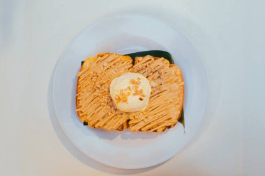 Düz karamelli tost ekmeği ve üzerine fındık serpilmiş beyaz tabakta vanilyalı dondurma.