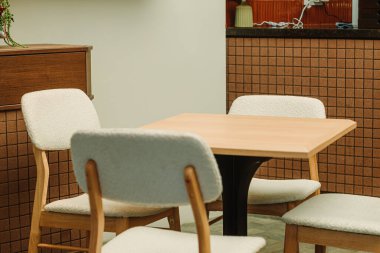 Dört yastıklı ahşap sandalye modern kapalı bir kafede kare bir ahşap masa etrafında düzenlenmiştir. Kahverengi döşeme tezgahı ve minimal dekorlu.