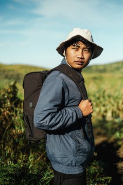 Doğu Cava, Endonezya 'daki Bromo Dağı' ndaki yemyeşil bir vadiyi keşfederken siyah bir sırt çantası taşıyan, mavi ceketli Güneydoğu Asyalı bir gencin yakın çekimi..