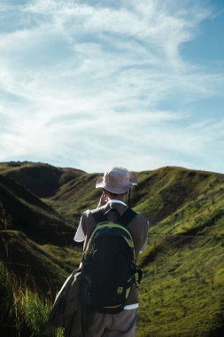 Kova şapkalı ve sırt çantalı Güneydoğu Asyalı bir yürüyüşçünün Bromo, Endonezya 'daki yemyeşil volkanik tepelerin tadını çıkarması maceranın ve vahşi doğadaki keşiflerin özünü yakalıyor..