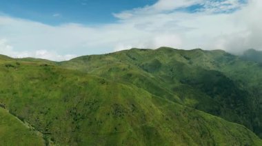Bukit Premium, East Java, Endonezya 'nın yeşil tepeleri ve vadileri üzerinde tarımsal teraslar ve açık mavi bir gökyüzü bulunan hava görüntüleri..
