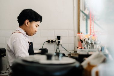 Beyaz gömlek ve siyah önlük giymiş genç bir Güneydoğu Asyalı şef profesyonel bir restoran mutfağında yemek hazırlıyor.