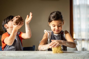İki kız kardeş evde beyaz masada yemek hazırlıyor.
