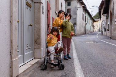 Birbiriyle konuşan iki kız ve bebek arabasında oturan küçük kız kardeş.