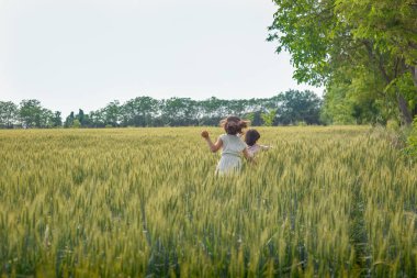 back view of two children with short dark hair walking away in wheat field