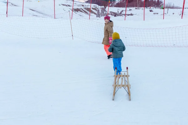 Två Barn Drar Träsläde Snöbacken Ljusa Kläder — Stockfoto