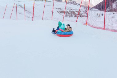 two children sledding on snow slope in one snow bob