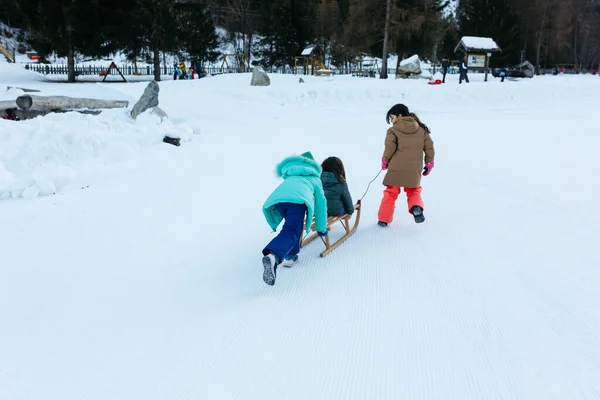 Two Girls Pulling Pushing Smaller Girl Wooden Sled Snow Hill — Fotografia de Stock