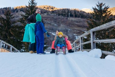 father talking to one child and other two daughters on snow slope with wooden sled