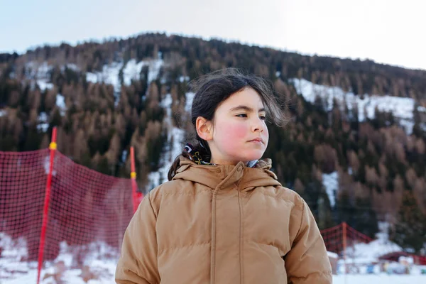 穿着棕色夹克的严肃姑娘站在多雪的山前的画像 — 图库照片