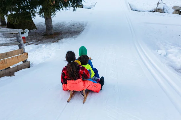 一群穿着鲜艳冬衣的孩子骑着一辆木制雪橇沿着雪坡滑行 — 图库照片