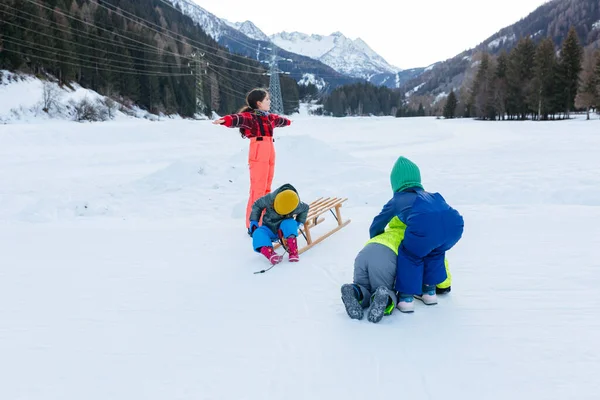 一群穿着鲜艳冬衣的孩子们在雪谷上与一只木制雪橇在森林和山地背景下玩耍 — 图库照片