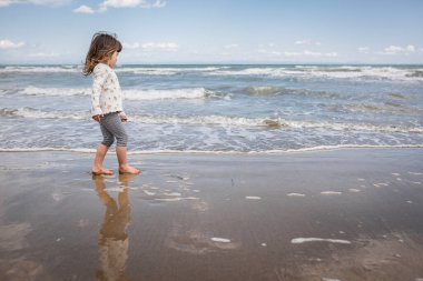 side view of little girl with brown hair walking along the sea coast on sand beach