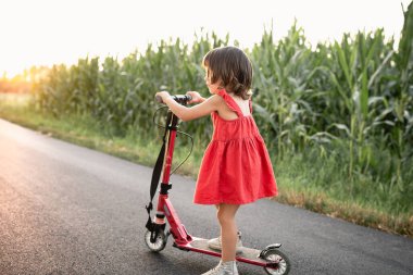 Kırmızı elbiseli kız kırmızı scooter kullanıyor.