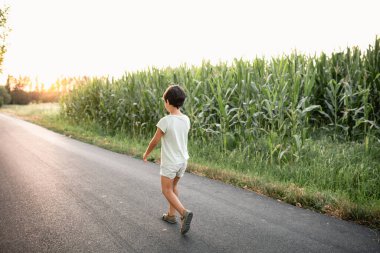 Koyu saçlı çocuğun dikiz aynasından mısır tarlasının yanındaki yolda yürürken.