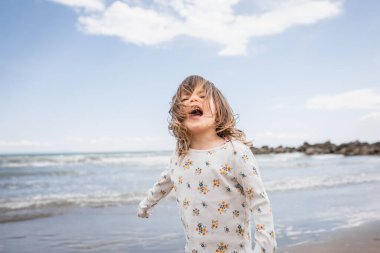 Kumsaldaki deniz kıyısında rüzgarla savrulan kahverengi saçlı küçük bir kız.
