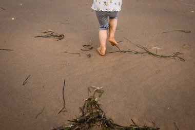 Çizgili kısa pantolonla kumsalda koşan çıplak ayaklı çocuk bacakları.