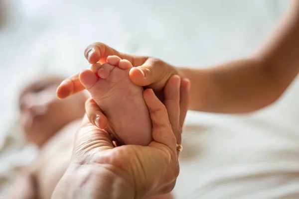hand of mother and elder sibling holding foot of newborn laying on the bed
