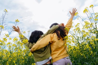 Alçak açı iki çocuğun sarı çiçeklerle birbirlerine sarılmalarını gösteriyor.