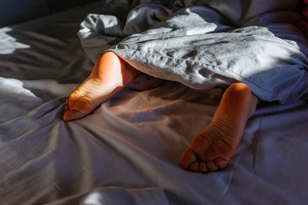 ベッドの早朝の明るい光の中で灰色の毛布の下の子供たちは裸足で — ストック写真