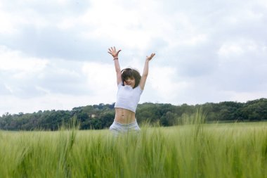 Kısa siyah saçlı, beyaz bluzlu, yeşil tarlada zıplayan komik kız.