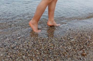 Yalınayak çocuk bacaklarına yaklaş. Gölün kıyısındaki taştan sahilde yürü.