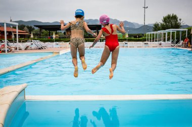 rear view of two girls in swimsuits jumping in the water in the pool