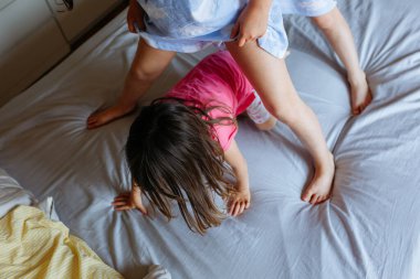 Yatakta duran ablaların bacaklarının üst görüntüsü ve büyük yatakta birlikte geçen küçük kız kardeş.