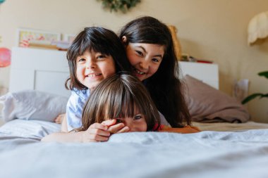 Üç gülümseyen çocuğun piramidi yatağın üzerinde yan yana yatıyor.