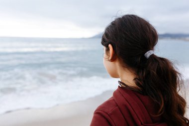 Sahilden denize bakan uzun saçlı kızın dikiz manzarası.