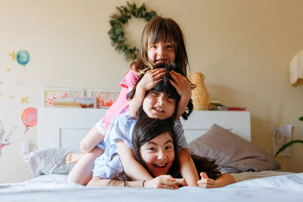 pyramid of three smiling children lying on each other on the bed